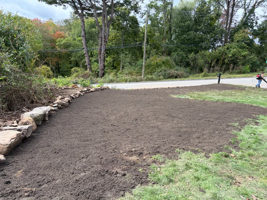 Cleared garden plot with freshly tilled soil and stone border beside a road.