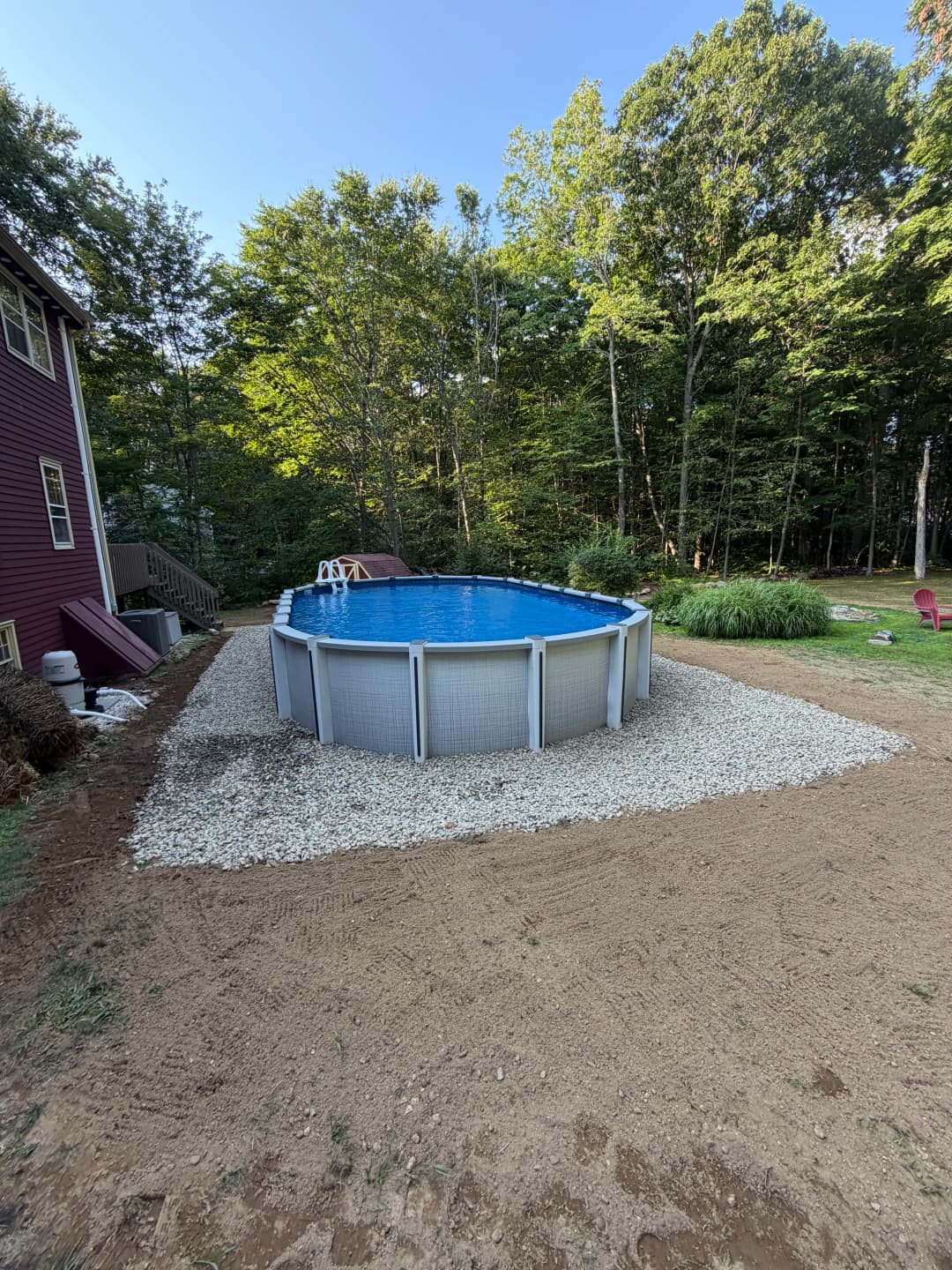 Above-ground swimming pool surrounded by gravel in a wooded backyard setting.