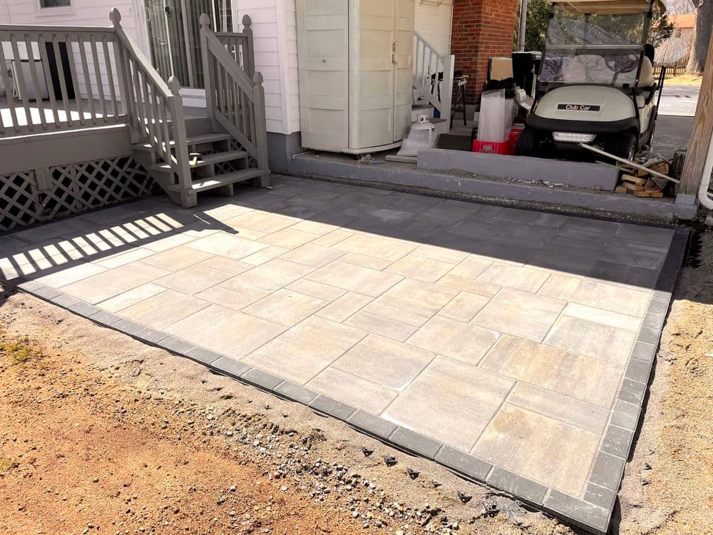 Patio installation with gray pavers and a new concrete border next to a house entrance.